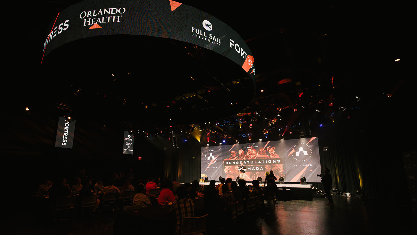 A wide shot of the Fortress’ interior filled with Armada athletes while the host stands on stage in front of a graphic that reads “Congratulations Armada”