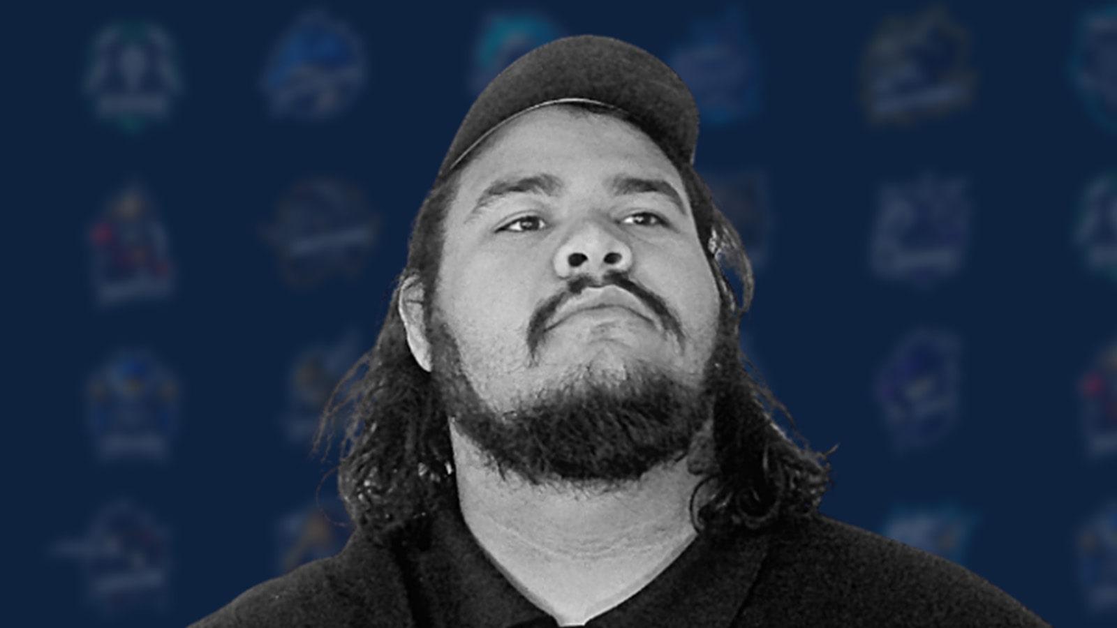 Chris “Fluffy” Aviles, a man with dark, shoulder-length hair and a black polo featuring the XP League logo against a blue backdrop featuring XP League branding.