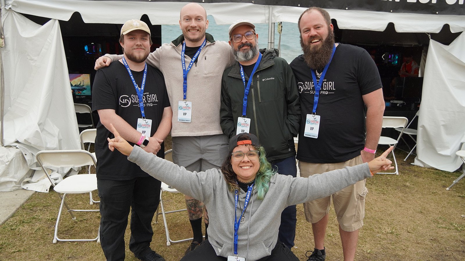 A group of five people standing in front of a large festival tent with rows of gaming computers set up inside.