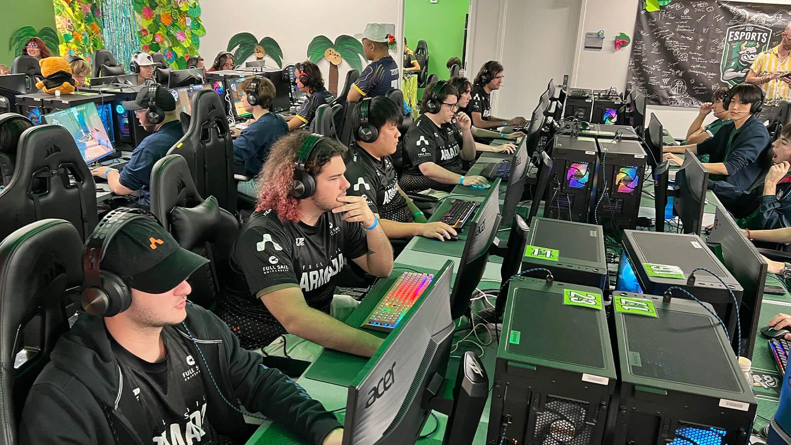 Dozens of Armada players sit in gaming chairs at desktop computers. They are wearing headphones and playing video games.