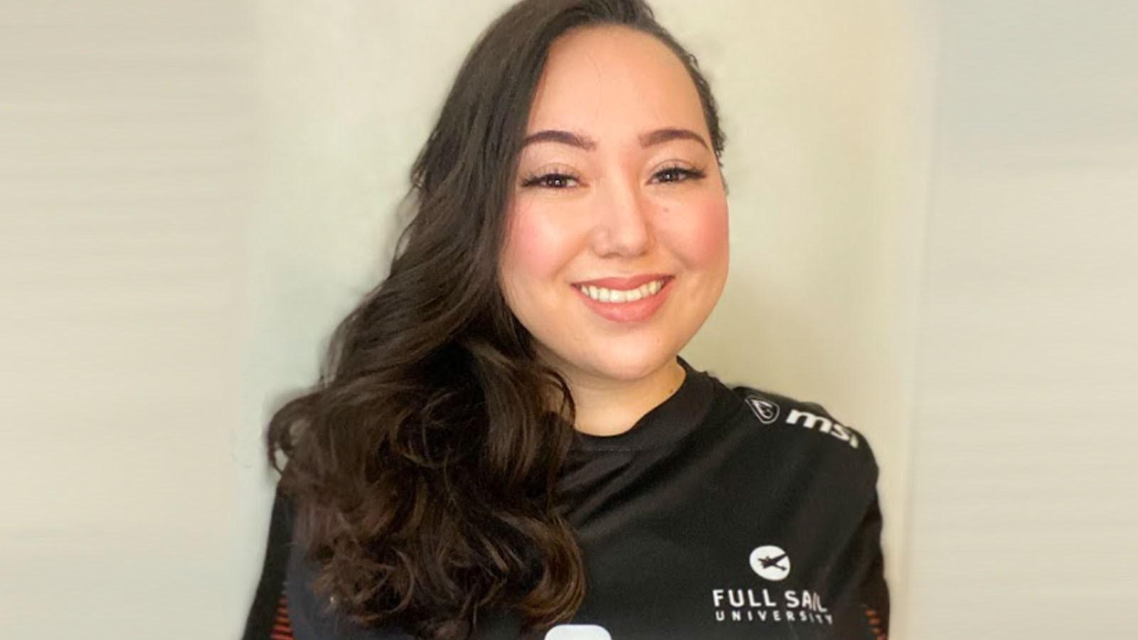 Grad Inetta Bennett, a woman with a big smile and long wavy brown hair to one side, wearing a Full Sail Armada branded esports jersey against a beige backdrop.