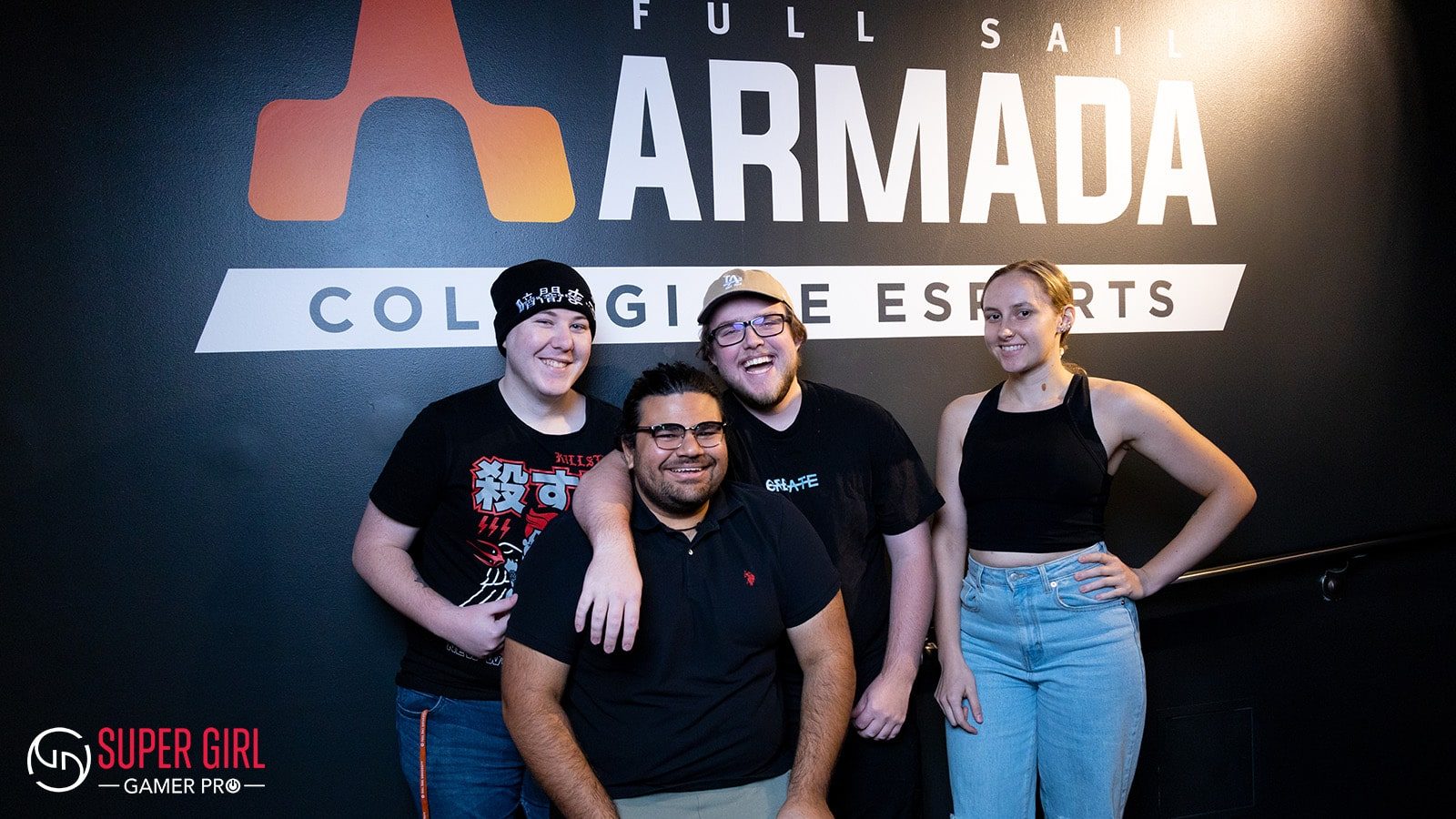 Full Sail students smiling while standing in front of the Full Sail Armada logo on campus, "Super Gamer Girl Pro" and logo appears in the bottom left corner.