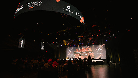 A wide shot of the Fortress’ interior filled with Armada athletes while the host stands on stage in front of a graphic that reads “Congratulations Armada”