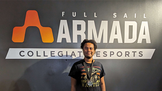 Full Sail Armada athlete Rajah wearing his second place medal while standing in front of a wall mural of the Armada logo.