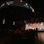 A wide shot of the Fortress’ interior filled with Armada athletes while the host stands on stage in front of a graphic that reads “Congratulations Armada”