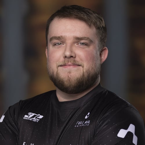 A man with short hair and a beard smiles confidently in a Full Sail Armada esports jersey.