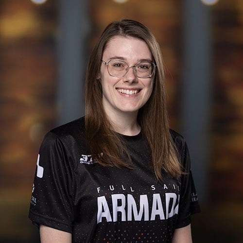 A smiling woman in glasses wears a Full Sail Armada jersey, standing in front of a warmly blurred background.